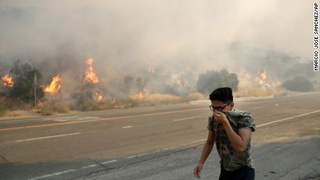 A man covers his face from the smoke created by a wildfire as he walks along Highway 14 Thursday, October 24, 2019, in Santa Clarita, California.