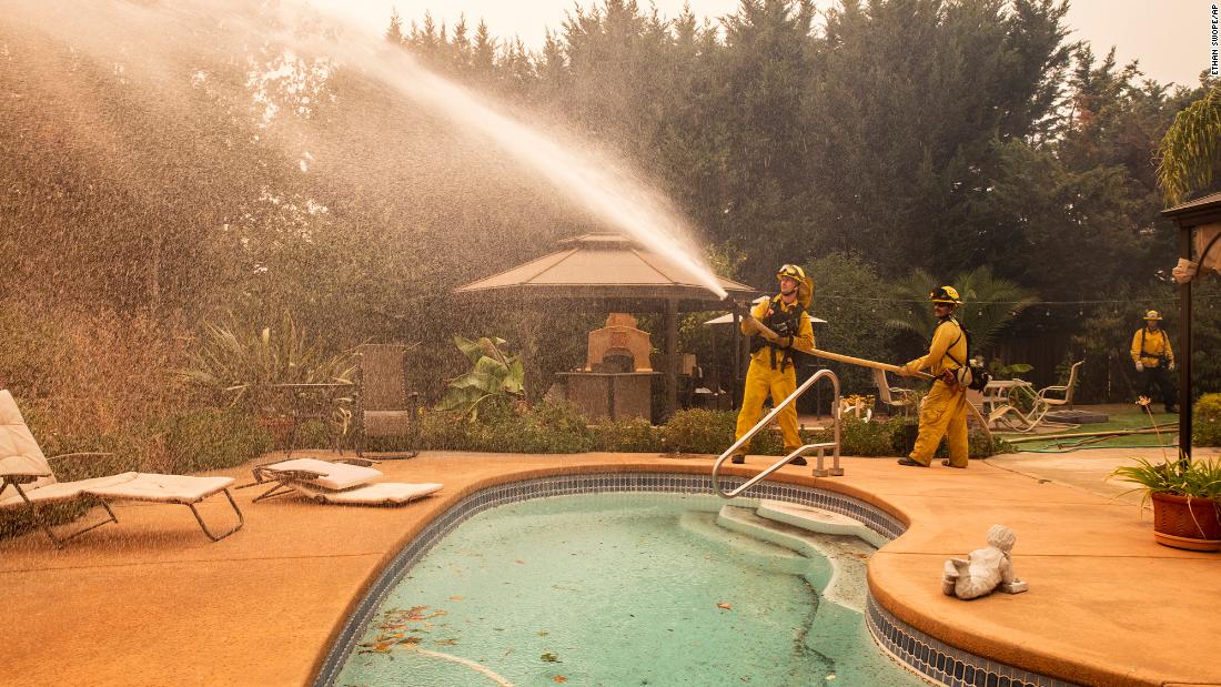 Firefighters battling the Kincade Fire spray water at a home in Windsor on Sunday, October 27.