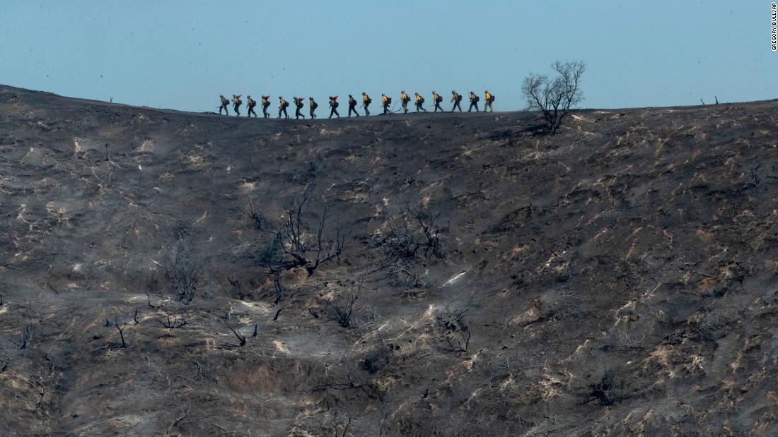 Fire crews walk along a blackened ridge as they battle the Getty Fire in Los Angeles.