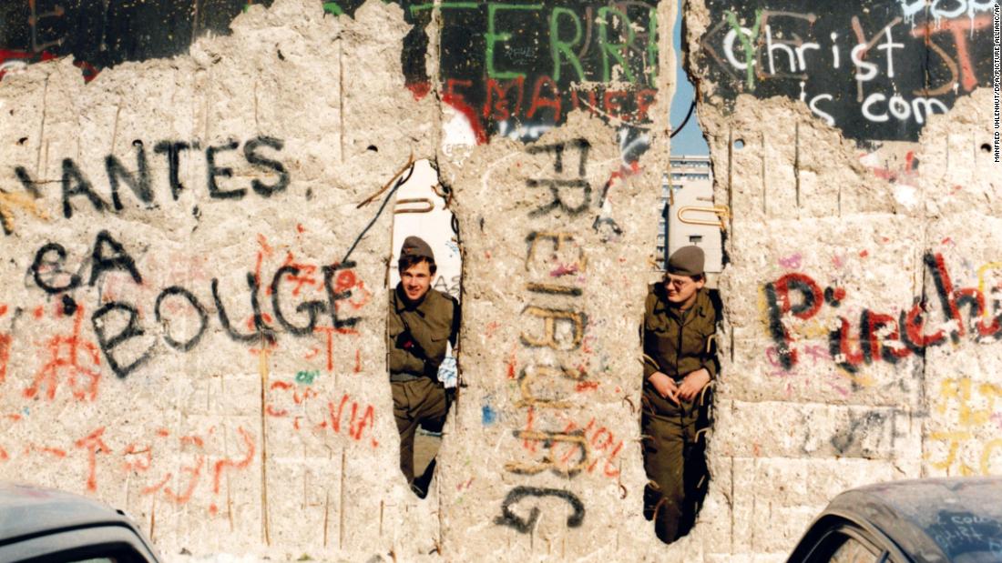 East German border guards peer through the damaged wall, near Checkpoint Charlie, in February 1990.  