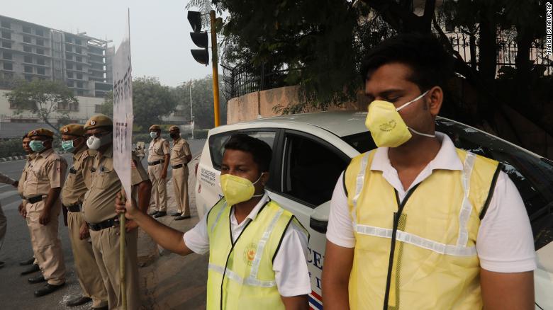 Volunteers and police wearing masks hold a banner urging drivers to obey the &quot;odd-even&quot; scheme.