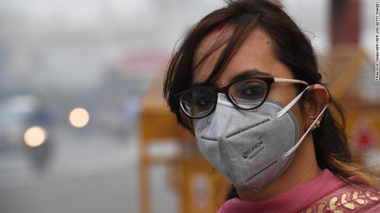 A woman wearing a protective face mask waits for a bus in smoggy conditions in New Delhi on November 4, 2019.