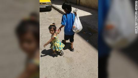 Yusuf holds the hand of his toddler sister Zahra as they walk down a street in Raqqa.