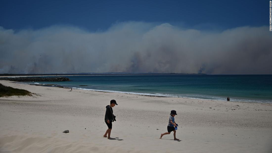 Fires burn in the distance as children play on a beach in Forster on November 9.