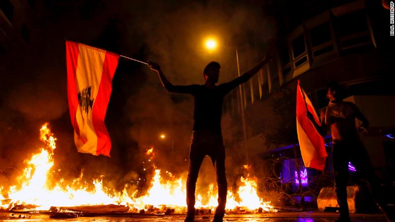 An anti-government protester holds a Lebanese flag in front of a barricade on fire on a road leading to the parliament building, during ongoing protests against the government, in Beirut, Lebanon, Wednesday, Nov. 13, 2019. 