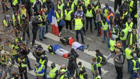 Protesters wrapped in French flags lie on the ground near riot police on the Champs Elysees on December 8, 2018.