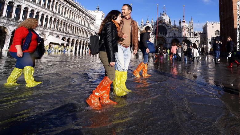 People wearing waterproof shoe covers walk through flood water at St. Mark&#39;s Square in Venice, Italy, on Thursday, November 14.