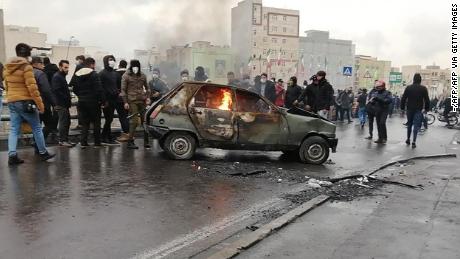 Iranian protesters gather around a burning car Saturday in the capital city of Tehran.