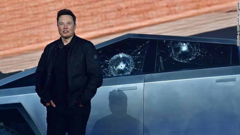 Tesla CEO Elon Musk stands in front of the shattered windows.