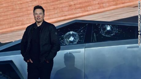 Tesla CEO Elon Musk stands in front of the shattered windows.