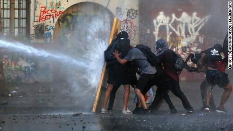 Demonstrators take cover from water fired by a riot police truck during a protest against President Sebastian Piñera on November 19 in Santiago, Chile.