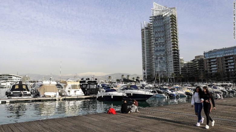 Women walk along a pier past moored boats in the Lebanese capital Beirut&#39;s Zaitunay Bay on January 24, 2019, with a view of the snow-covered mountain of Sannine overlooking the city in the background.