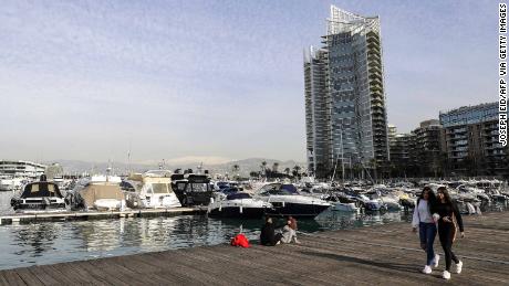 Women walk along a pier past moored boats in the Lebanese capital Beirut&#39;s Zaitunay Bay on January 24, 2019, with a view of the snow-covered mountain of Sannine overlooking the city in the background.