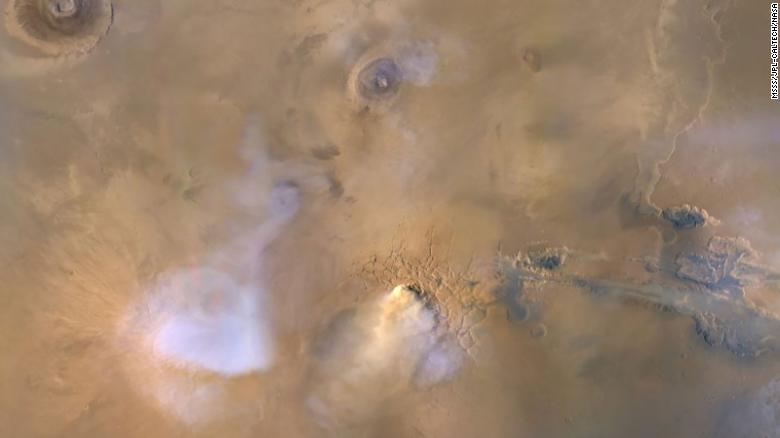 The cloud in the center of the image is actually a dust tower that occurred in 2010 and was captured by the Mars Reconnaissance Orbiter. The blue and white clouds are water vapor.