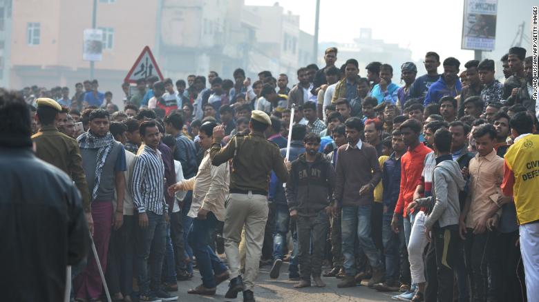 Police personnel try to clear a road as onlookers gather near the factory fire.