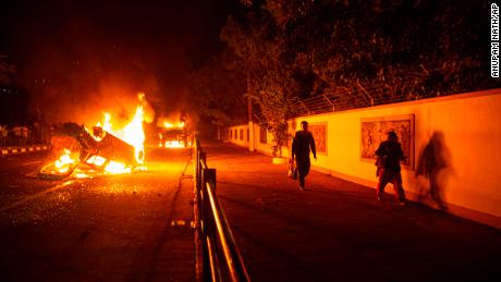 People walk past vehicles set on fire by demonstrators protesting against the Citizenship Amendment Bill (CAB) in Guwahati, India, Wednesday, December 11, 