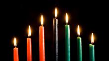 Medium shot of Kwanzaa candles lit against a black background with room for text.