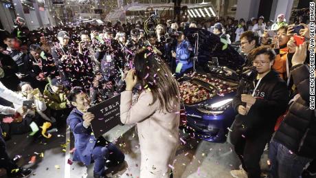 An employee, left, proposes to his girlfriend with his newly delivered Tesla Model 3 in Shanghai on Monday.