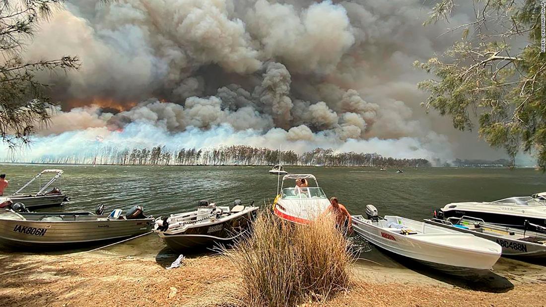 Boats are pulled ashore as smoke and wildfires rage on January 2 behind Lake Conjola.