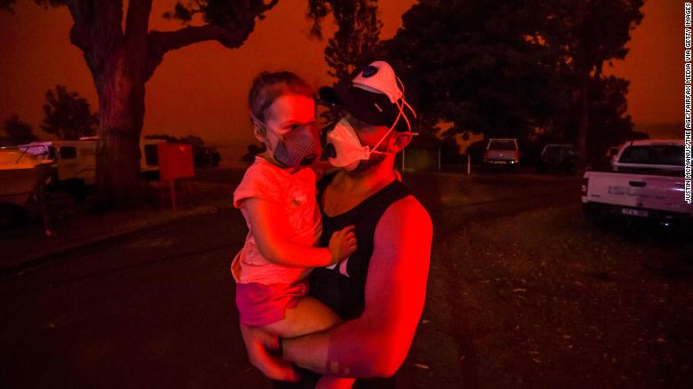 A father holds his daughter as the skies above turn red during the day on January 4 in Mallacoota, Australia. Many parents with young children were stuck in Mallacoota after flights were grounded because of smoke and only school-aged children and older were allowed to evacuate by boat. 