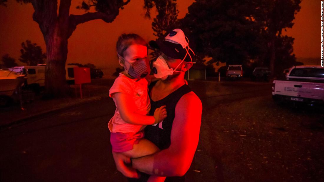 A father holds his daughter as the skies above turn red during the day on January 4 in Mallacoota, Australia. Many parents with young children were stuck in Mallacoota after flights were grounded because of smoke and only school-aged children and older were allowed to evacuate by boat. 