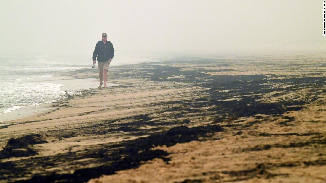 A man walks past ash from bushfires washed up on a beach in Merimbula on January 5.