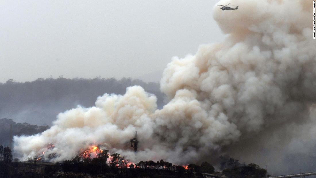 A military helicopter flies above a burning woodchip mill in Eden, New South Wales, on January 6.