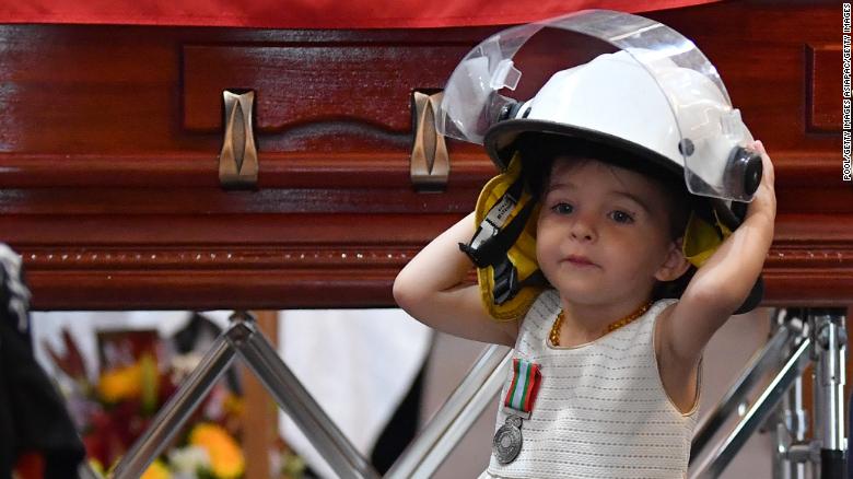 Charlotte O&#39;Dwyer, the young daughter of Rural Fire Service volunteer Andrew O&#39;Dwyer, stands in front of her father&#39;s casket wearing his helmet.