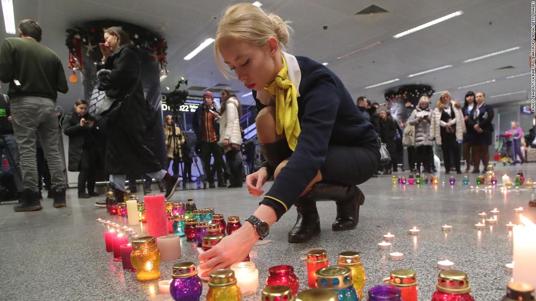 A Ukraine International Airlines employee lights a candle that is part of a symbolic runway at the airport memorial.