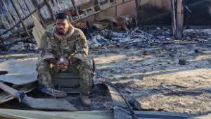Staff Sergeant Akeem Ferguson sits between charred metal at the site of the destroyed housing unit for drone pilots and operators.