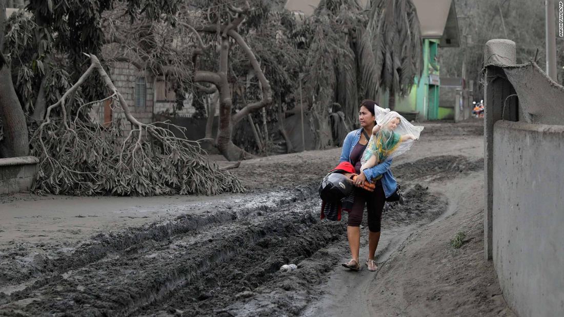 Leila de Castro carries a religious statue recovered from a family member's house as she walks along an ash-covered road in Boso-Boso on January 14.