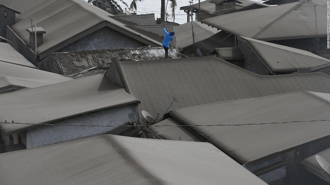 A resident cleans ash from his roof in Agoncillo on Tuesday, January 14.