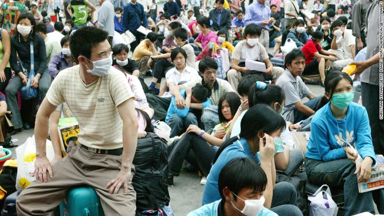 Migrant workers in face masks wait outside the train station in Guangzhou, China, before returning home during the SARS outbreak in 2003.