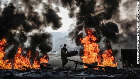 A Lebanese man throws a tyre on a burning barricade during an anti-government protest on October 17,  2019.