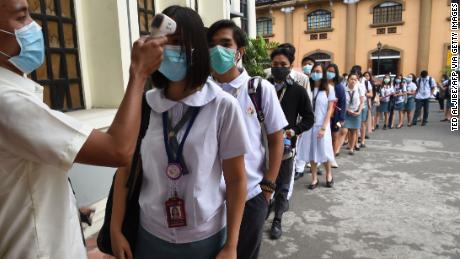 Students wearing protective face masks have their temperatures taken while entering their college campus in Manila.