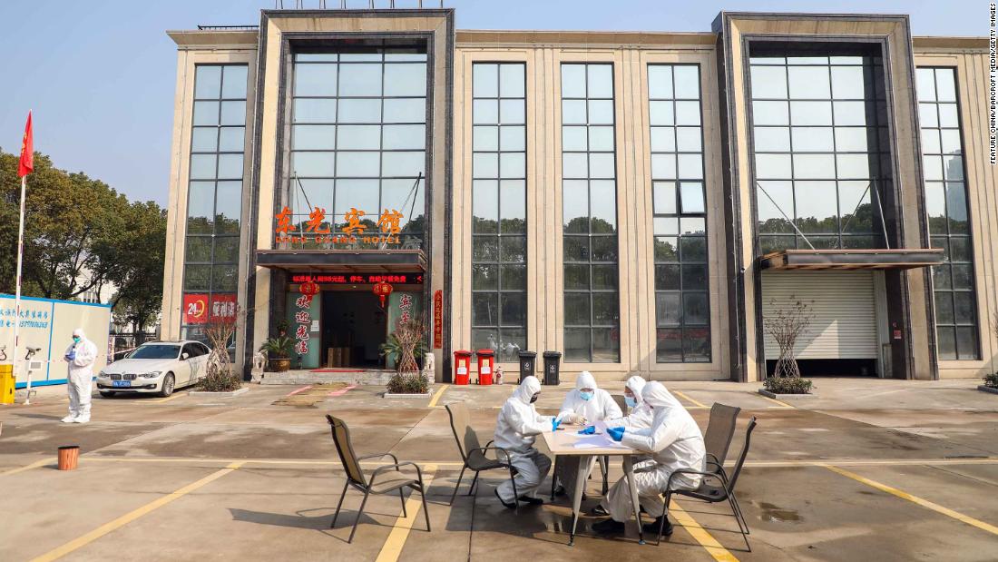 People wearing protective overalls talk outside a Wuhan hotel housing people in isolation on February 3, 2020.