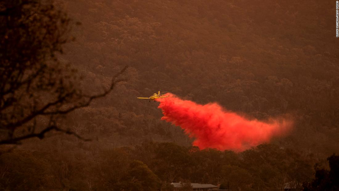 An airplane dumps fire retardant behind houses at the foot of Mount Tennent as  fire creeps through the Namadgi National Park in Canberra on Thursday, January 30.