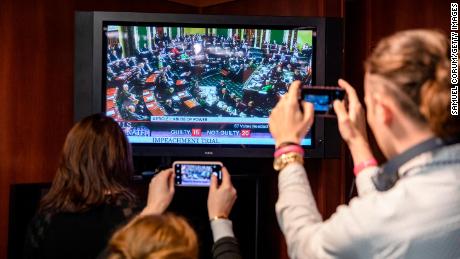 Reporters take photos of the television as they watch the Senate vote on whether to acquit President Donald Trump.
