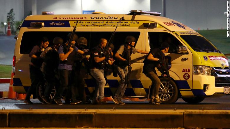 Thailand security forces take cover behind an ambulance as they chase a shooter thought to be hiding in a shopping mall after a mass shooting in Thailand.