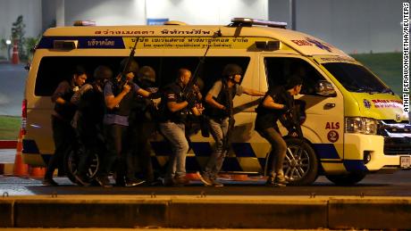 Thailand security forces take cover behind an ambulance  as they chase a shooter thought to be hiding in a shopping mall after a mass shooting in Thailand.