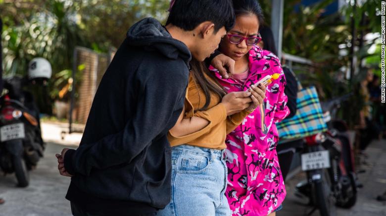 Thai people check the news on a phone near the shopping mall where a mass shooting took place on Saturday in Korat.