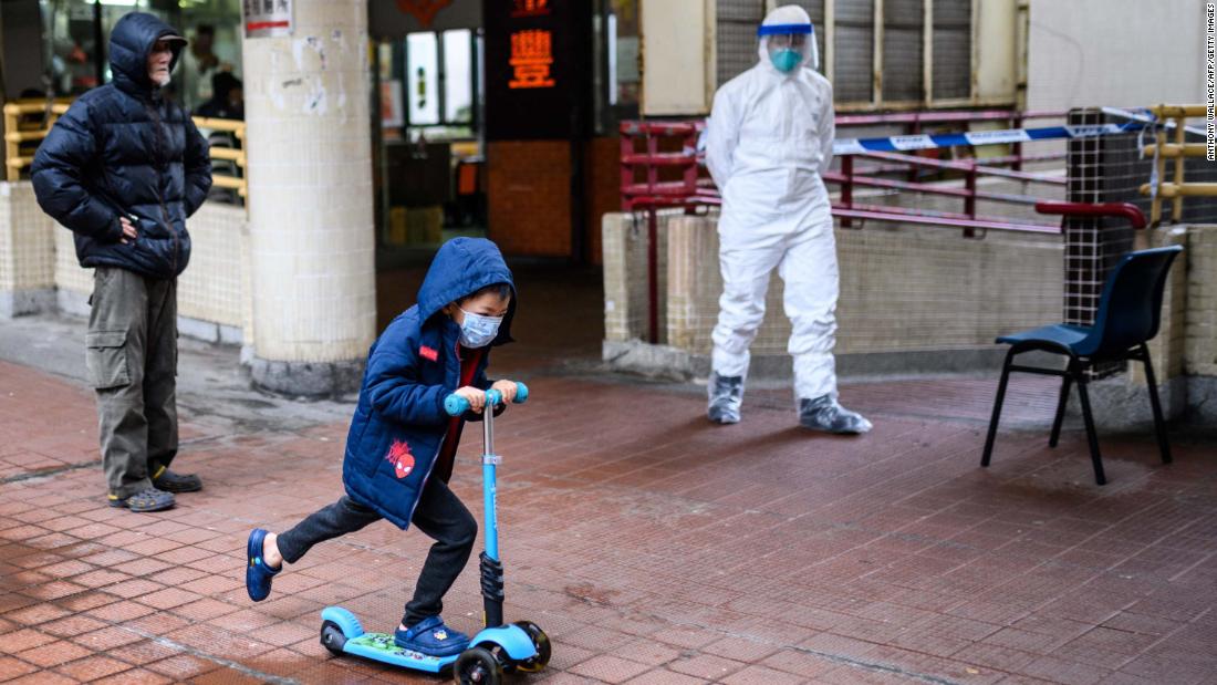 A child rides a scooter past a police officer wearing protective gear outside the Hong Mei House in Hong Kong. More than 100 people evacuated the housing block after four residents in two different apartments tested positive for the coronavirus.