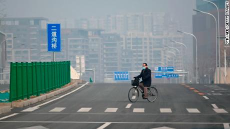 A man wearing a face mask rides his bicycle along an empty street in Beijing on February 12, 2020.