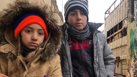 The kids wait patiently and without complaint outside their house in the last opposition-held territory in Syria, as their mother packs their belonging in the back of a truck.