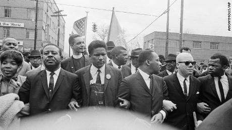 Martin Luther King Jr. cierra los brazos con sus ayudantes mientras marcha al juzgado en Montgomery, Alabama, el 17 de marzo de 1965. John Lewis está en el extremo derecho. 