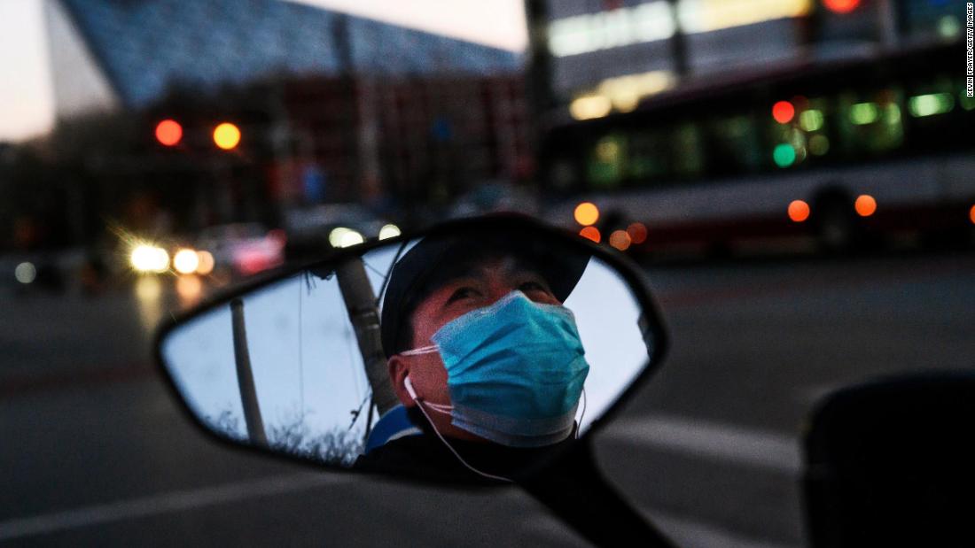 A Chinese man is seen in the side mirror of his scooter as he wears a protective mask in Beijing on February 22. More than 780 million people across China -- nearly half the country&#39;s population -- are still under some kind of travel restriction. These restrictions range from complete lockdowns, to limited entry in and out of certain neighborhoods.