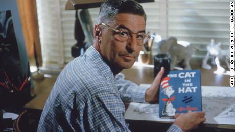 American author and illustrator Dr Seuss (Theodor Seuss Geisel, 1904 - 1991) sits at his drafting table in his home office with a copy of his book, &#39;The Cat in the Hat&#39;.