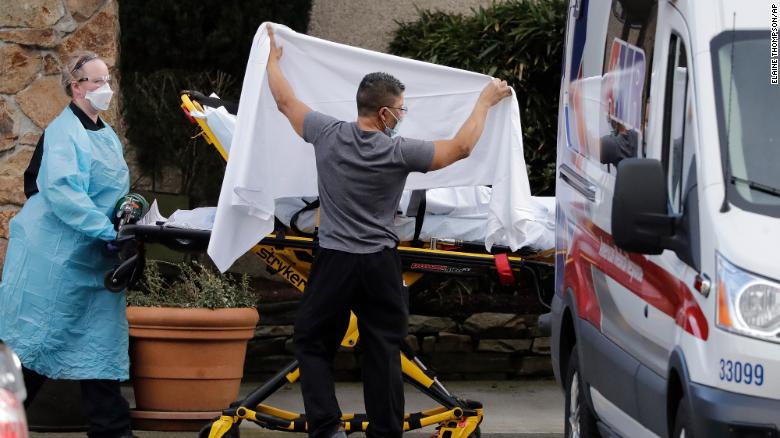 A staff member blocks the view as a person is taken by a stretcher to a waiting ambulance from a nursing facility where more than 50 people are sick and being tested for the coronavirus. 