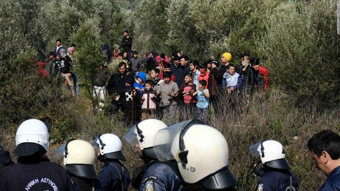 Migrants look on as police block a road near the Moria refugee camp.