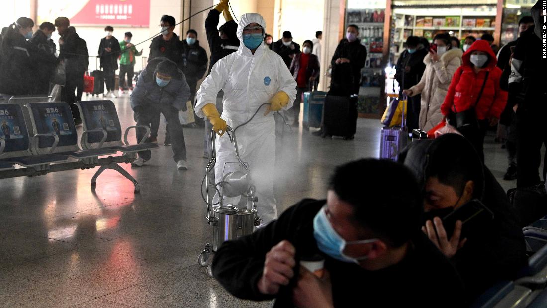 Passengers react as a worker wearing a protective suit disinfects the departure area of a railway station in Hefei, China, on March 4.